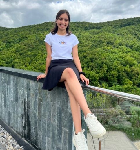 photo of student sitting on a railing smiling near the mountains 