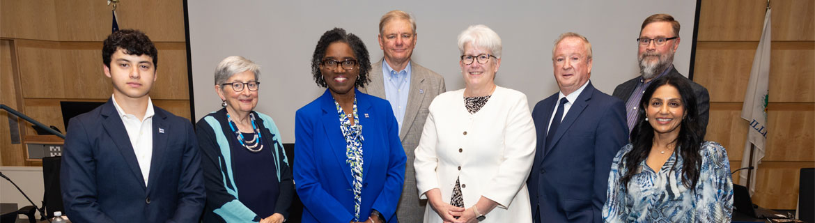 Group photo of eight board members standing in a conference room at Harper College.