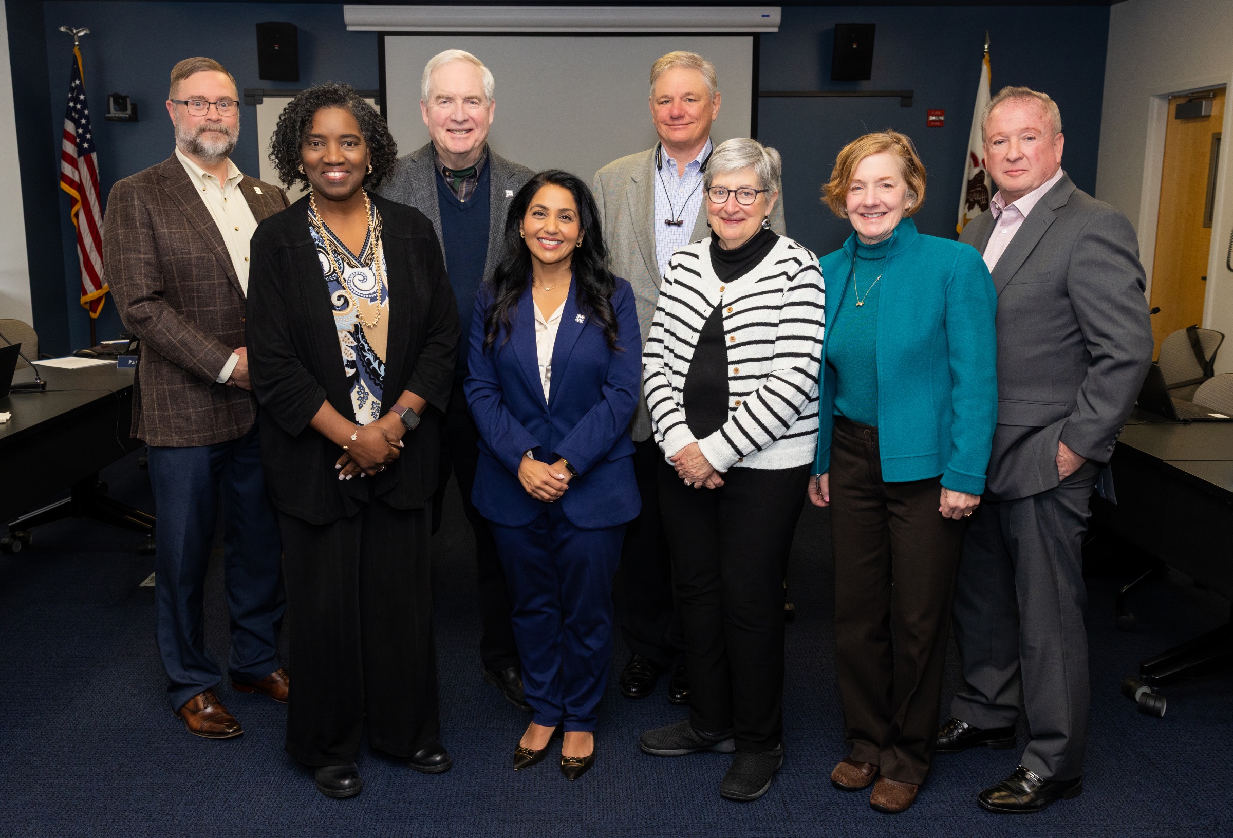 Group photo of eight board members standing in a conference room at Harper College.