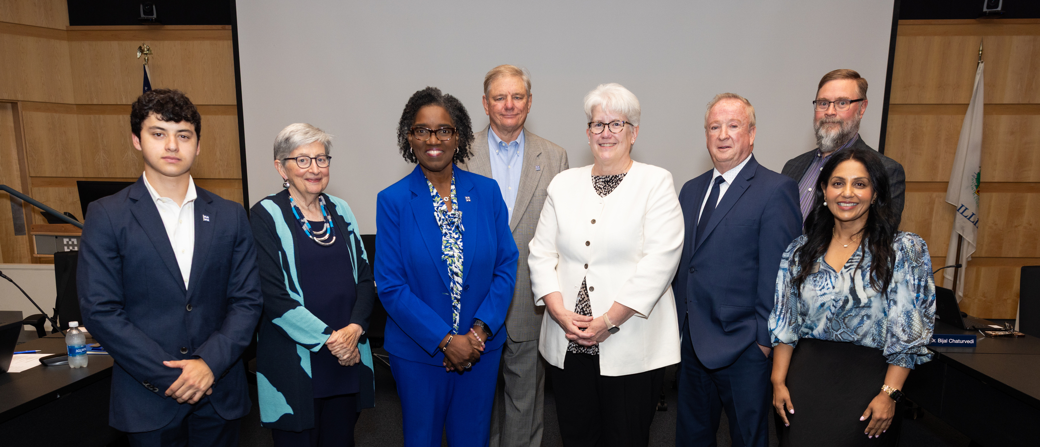 Group photo of eight board members standing in a conference room at Harper College.