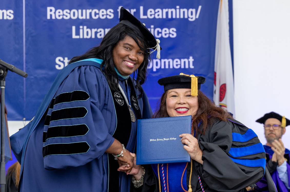 Dr. Proctor posing with a Harper graduate with her diploma at graduation ceremony.