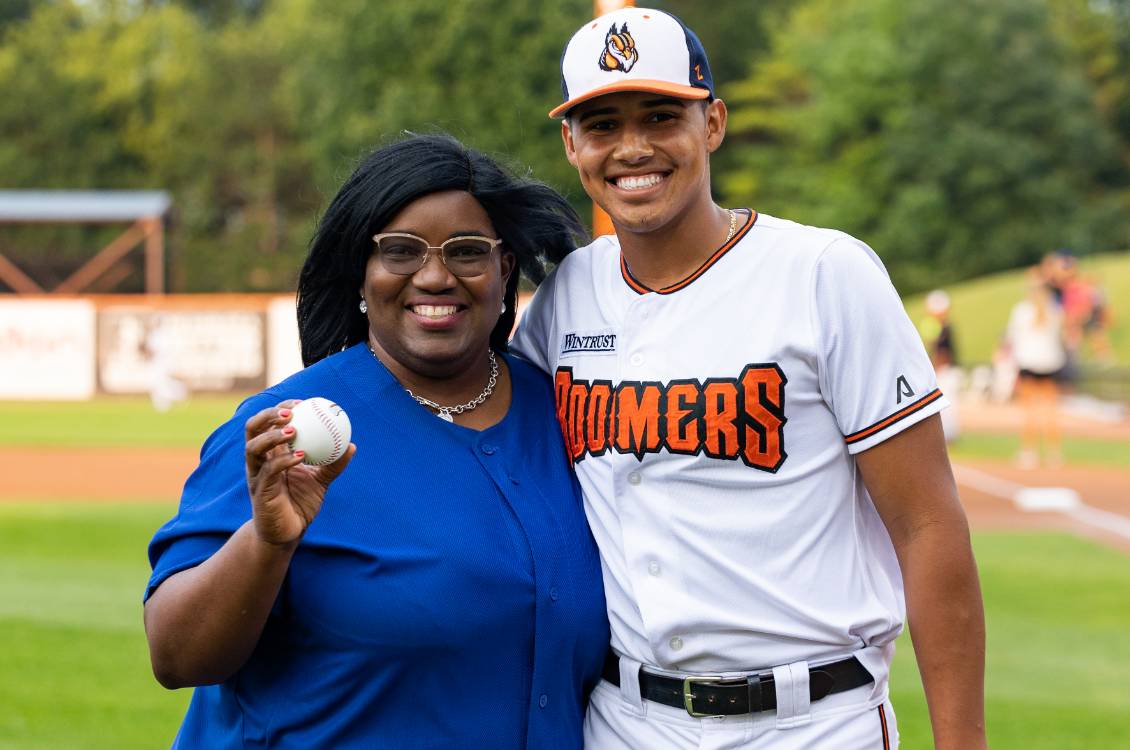 Dr. Proctor holding a baseball standing with Boomers baseball player at a game.