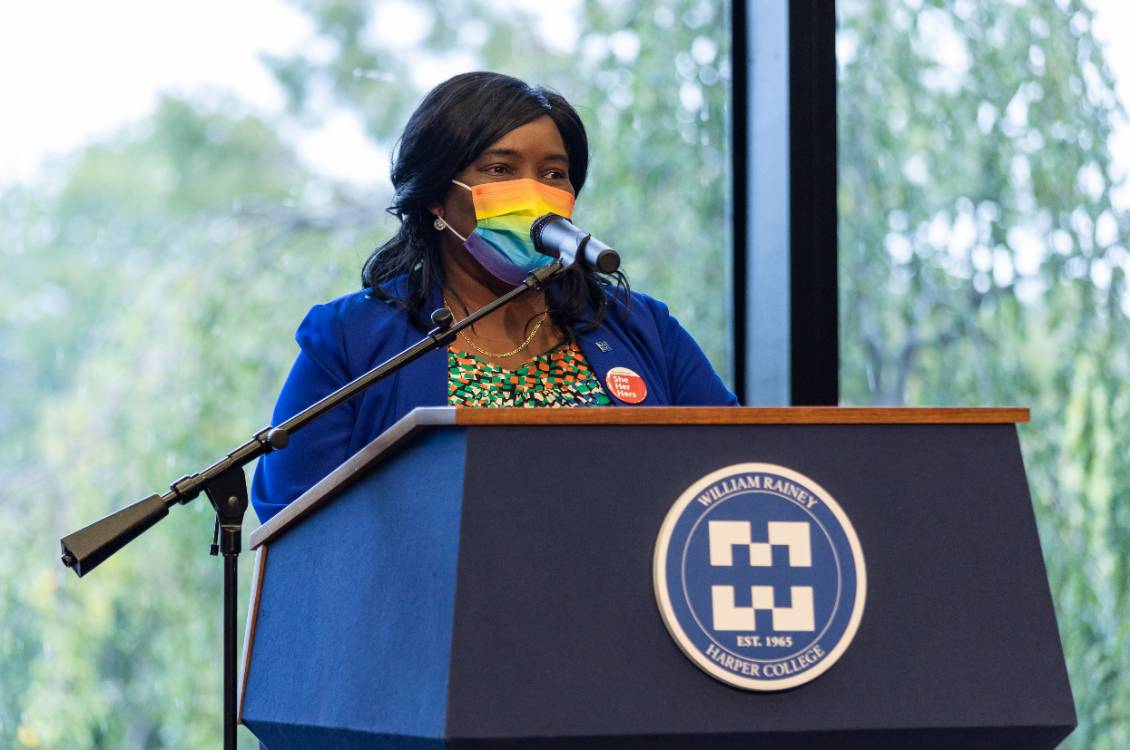 Dr. Proctor giving a speech at a podium wearing a rainbow colored mask.