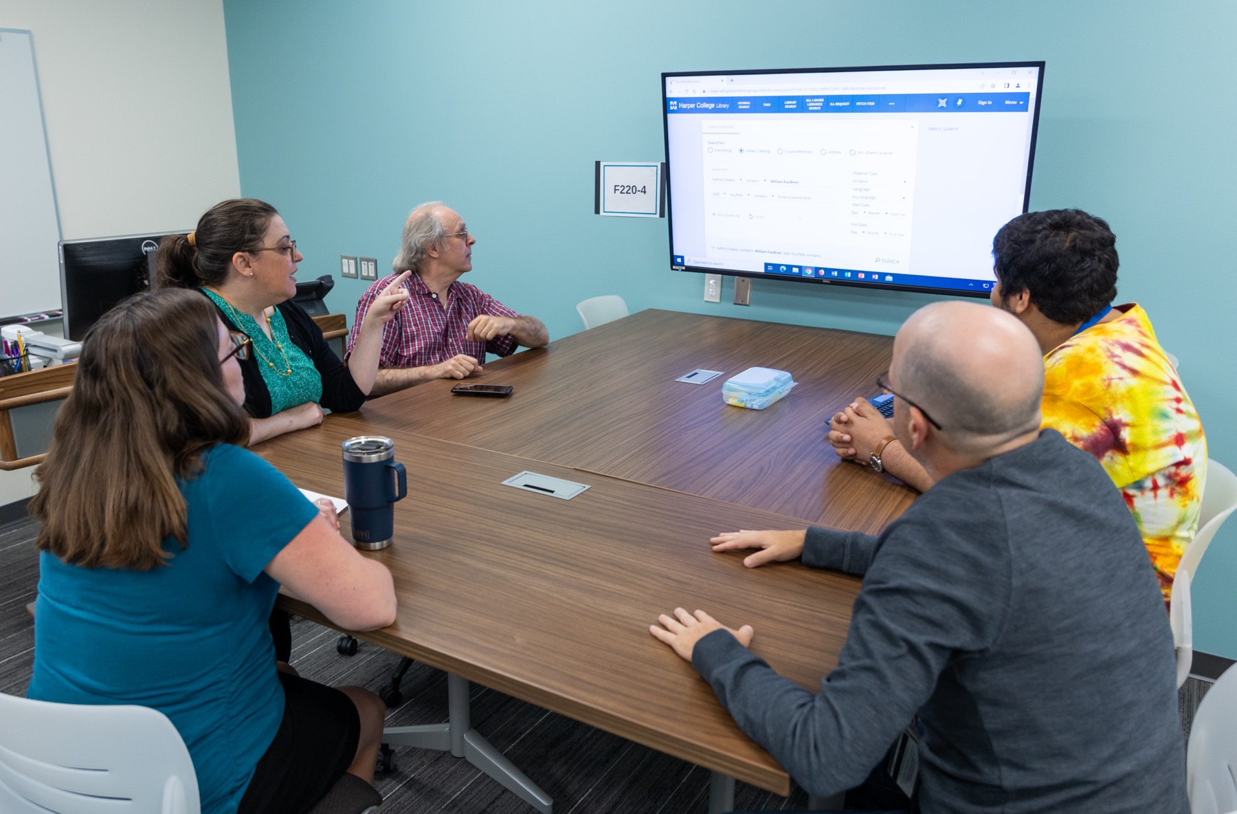 Group of people around a table looking at a screen on the wall 