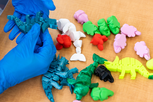 a gloved hand holding 3D printed dinosaurs