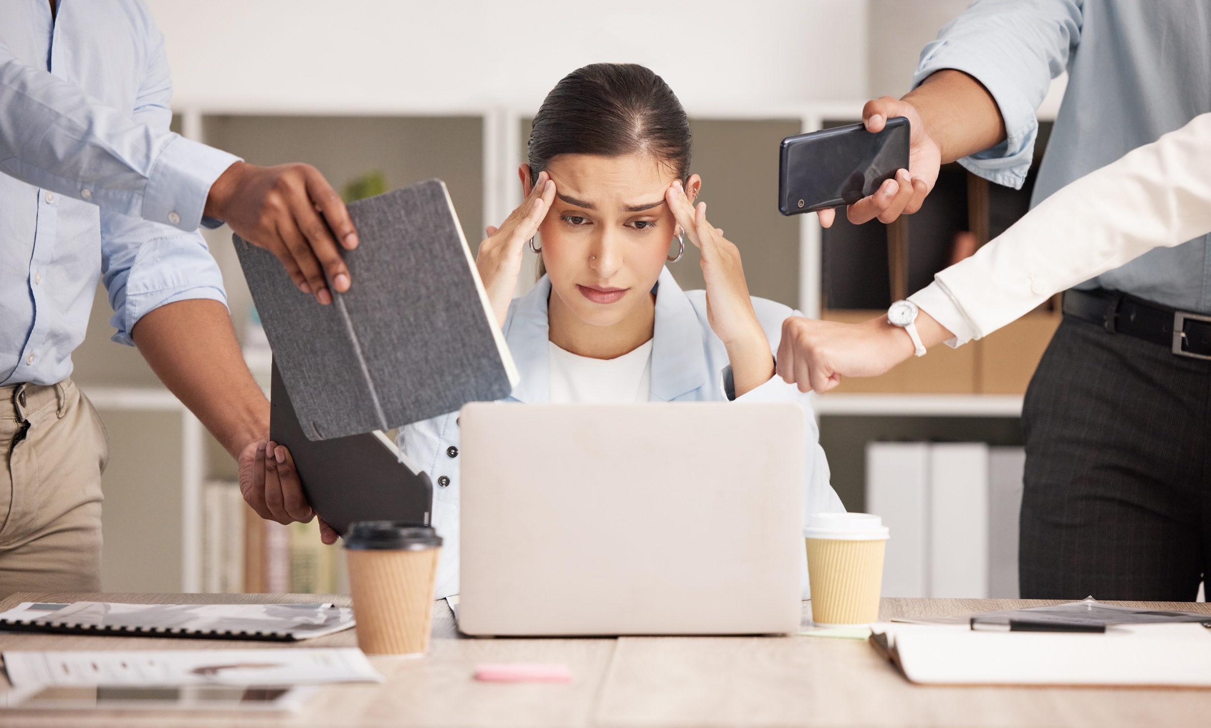 Stressed woman holding her head as others show her their phone and tablet screens.