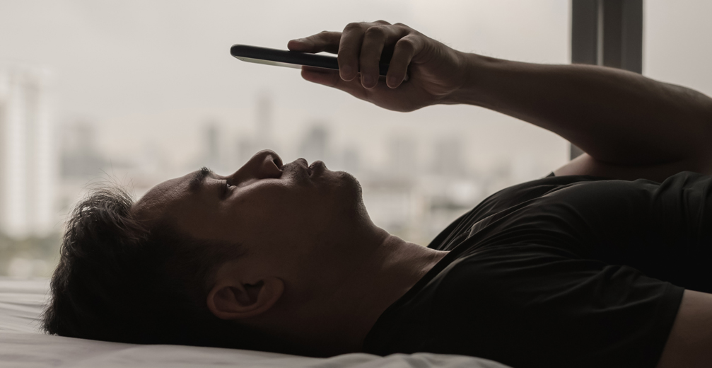Man lying on bed staring at phone