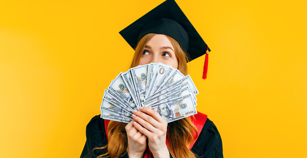 Woman in graduation cap with money fanned out in front of her face