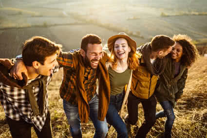 Group of young adults walking and laughing shoulder to shoulder through a hay field. 