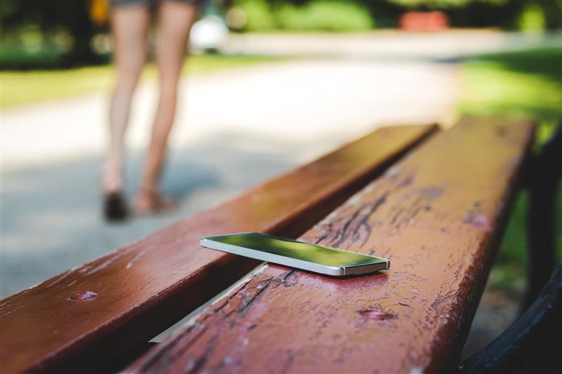 A person leaving their phone on a park bench, and walking away to disconnect from it.