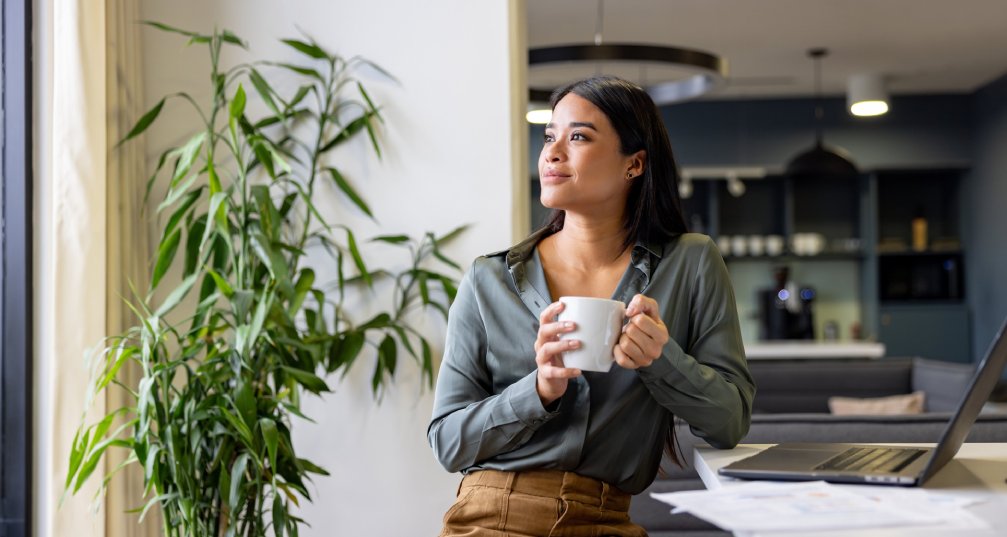 Woman holding a coffee cup and looking out the window of her home office.