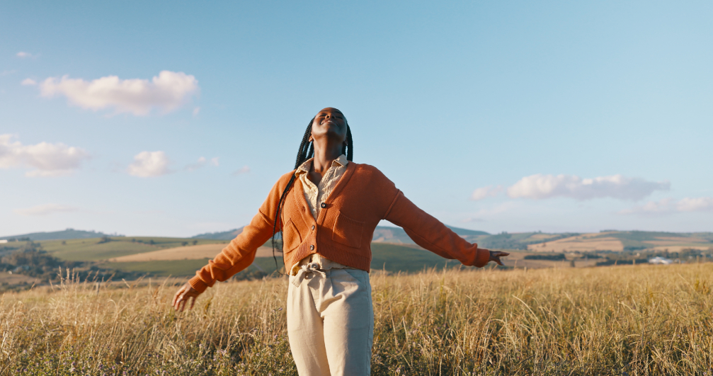 Woman feeling grateful in an open field. a woman stretches outside in the sun, feeling at peace