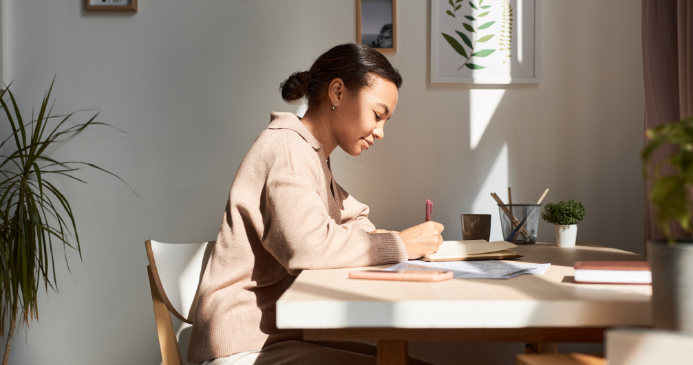 Young woman writing in her gratitude journal. a woman sits at her desk in her house, writing in her gratitude journal