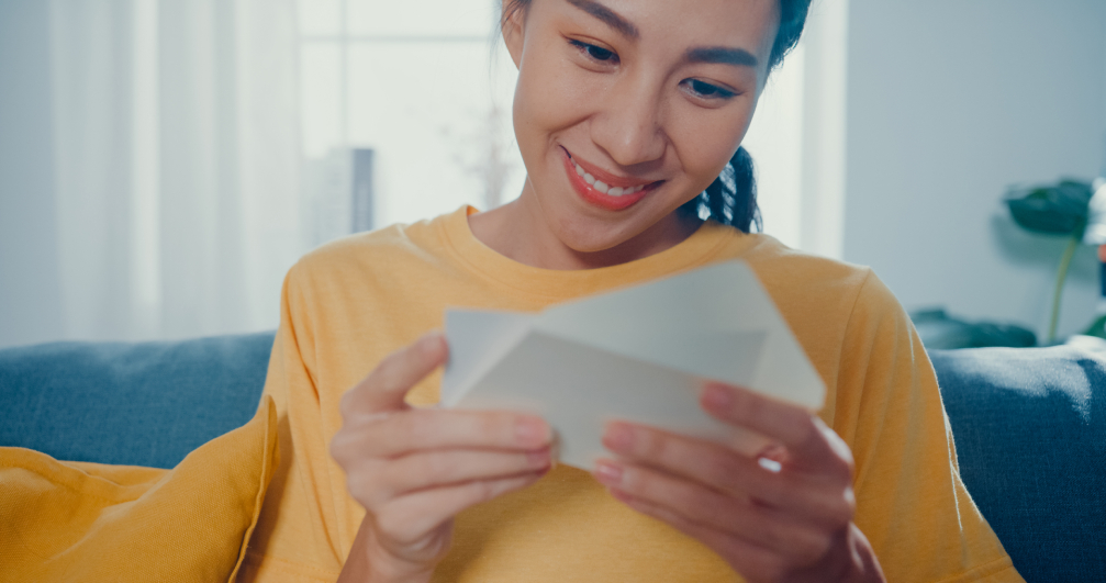 Young woman reading a letter from a loved one. a woman opening an envelope containing a thank-you card she recieved from a loved one