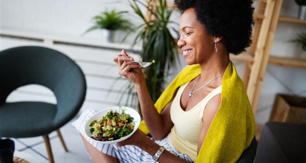 A woman seated and happily eating a healthy salad.