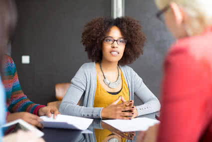 Female student sitting at table listening intently on a conversation on the other side of the table.