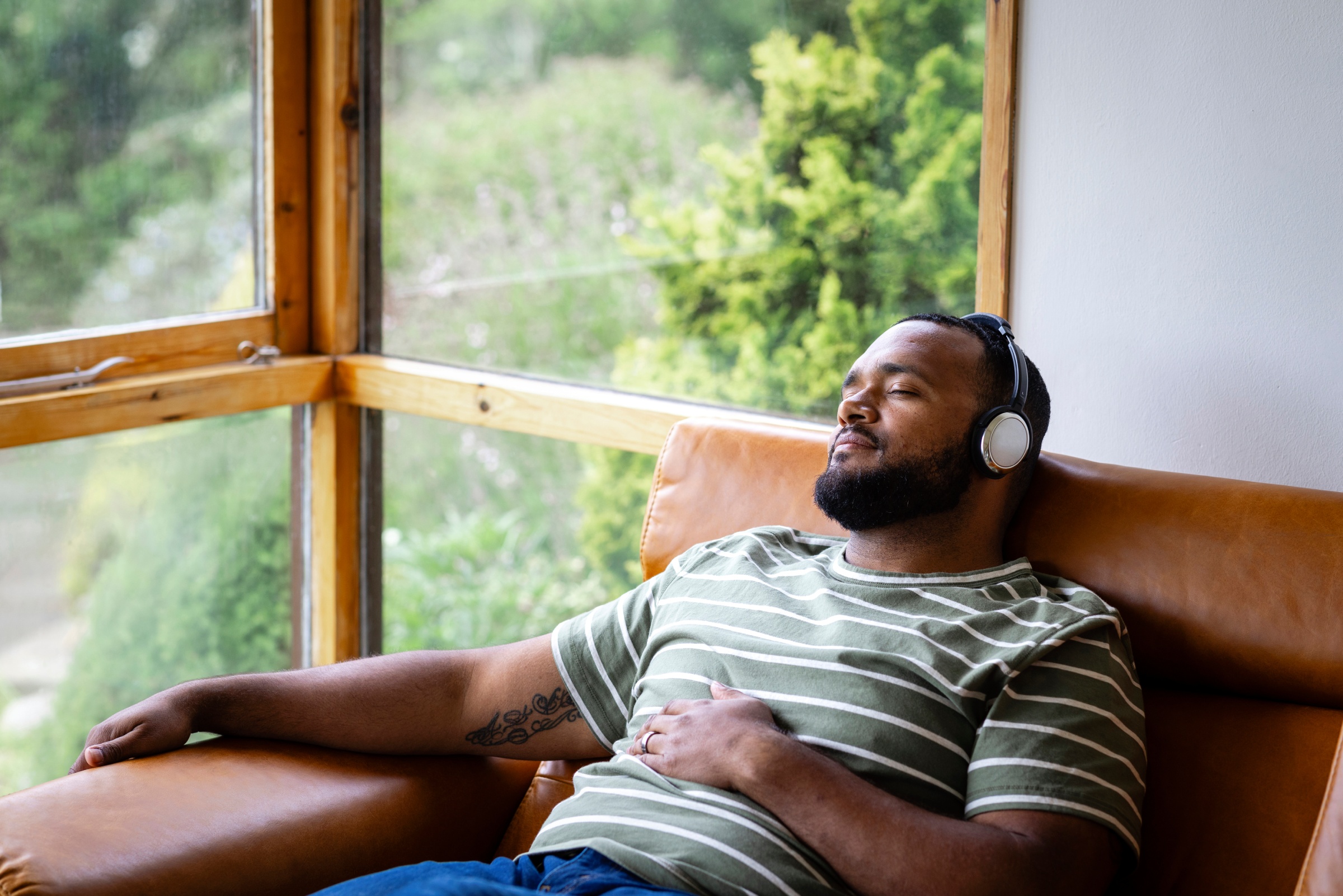 Man wearing headphones and relaxing in a chair by the window with sunlight peeking in.