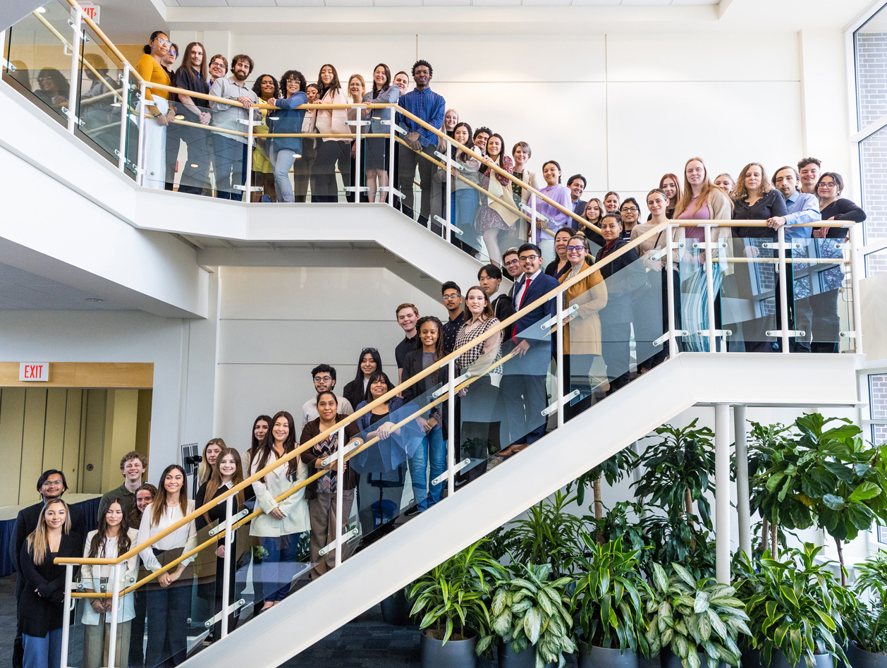 A large group of students (former scholarship recipients) standing in a group along a staircase and smiling 