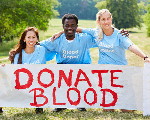 Photo of three people wearing "Donate Blood" T-Shirts holding banner that reads "Donate Blood"
