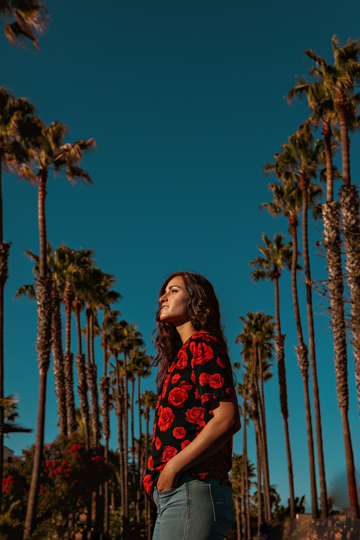 Photo of Angie K. standing outdoors with rows of palm trees in background