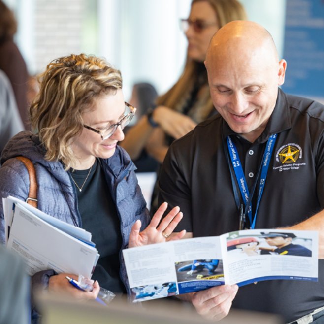 A prospective student looks over a pamphlet with a Harper representative