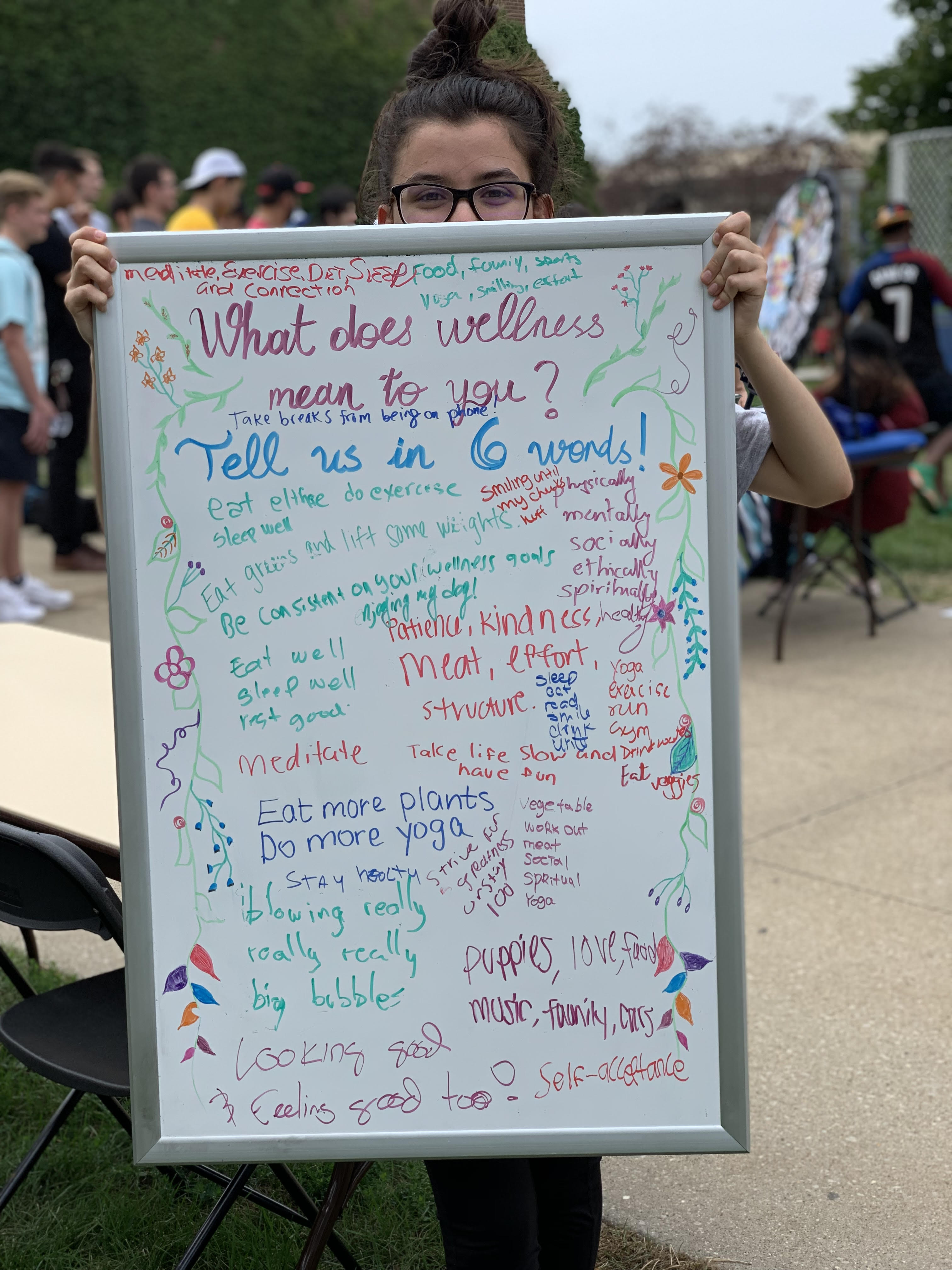 Photo of student holding up a white board with writing from various people about what wellness means to them.