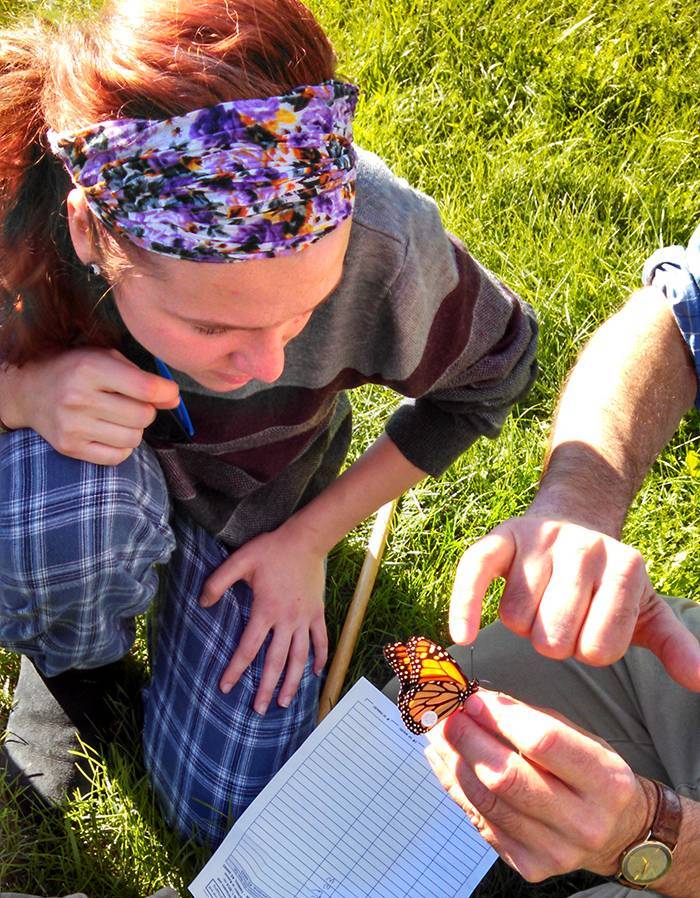 A teacher holds a butterfly, while a student looks on.