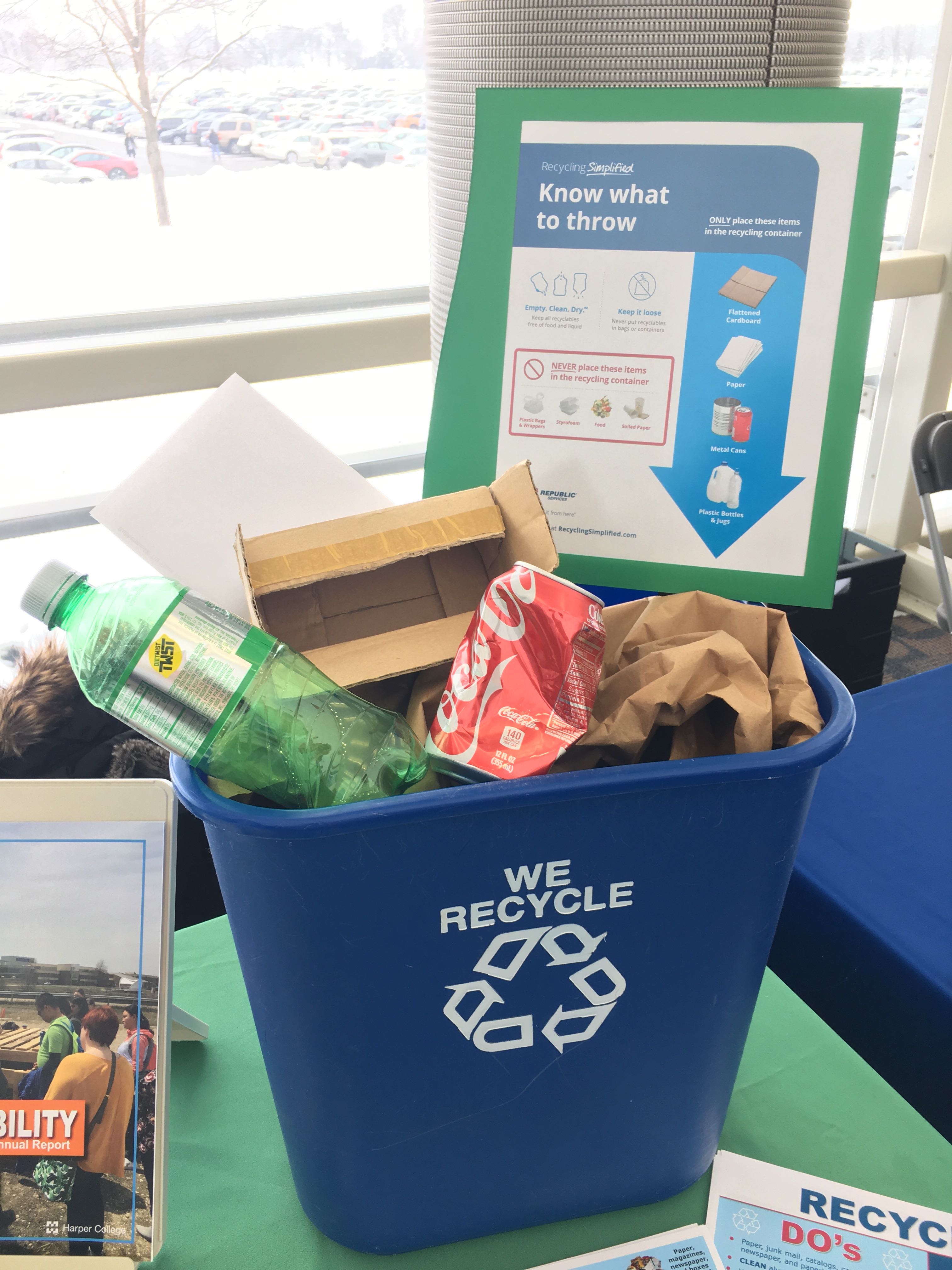A recycling bin filled with recyclables sits on a table.