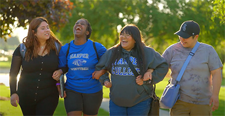 Students walk arm in arm, smiling and laughing on Harper's campus