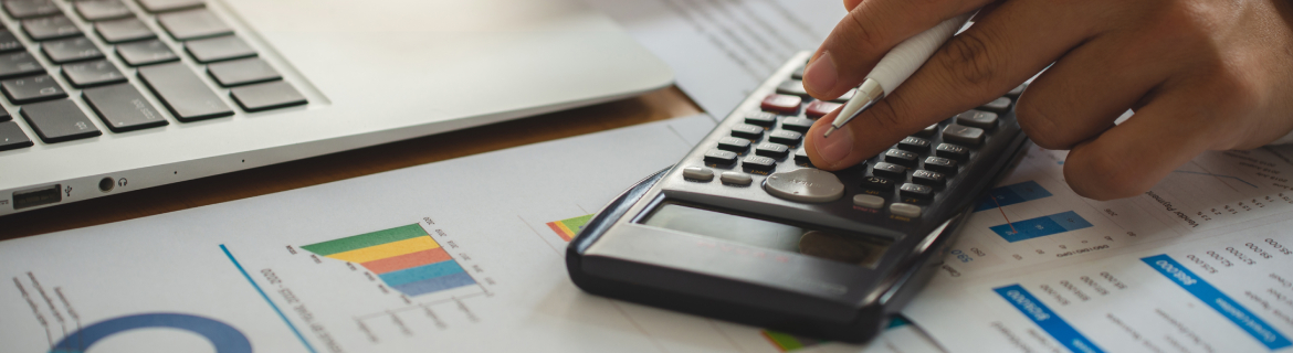 a calculator sits on a table with scattered papers, while a person calculates their budget