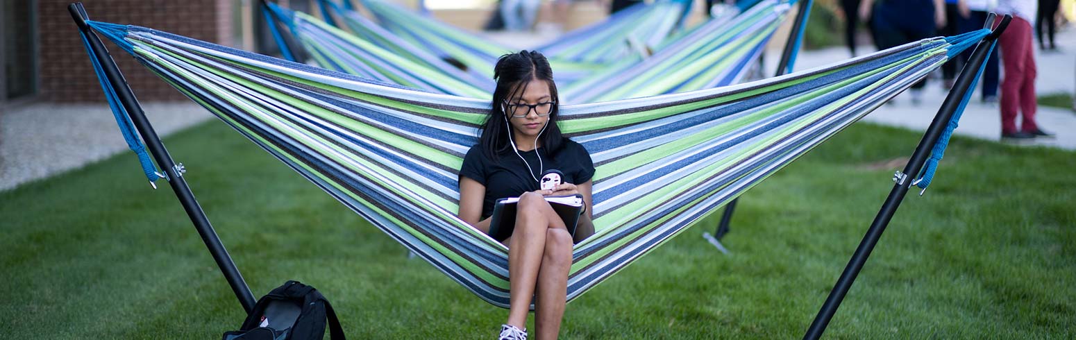 Student reading book while sitting in hammock on campus photo