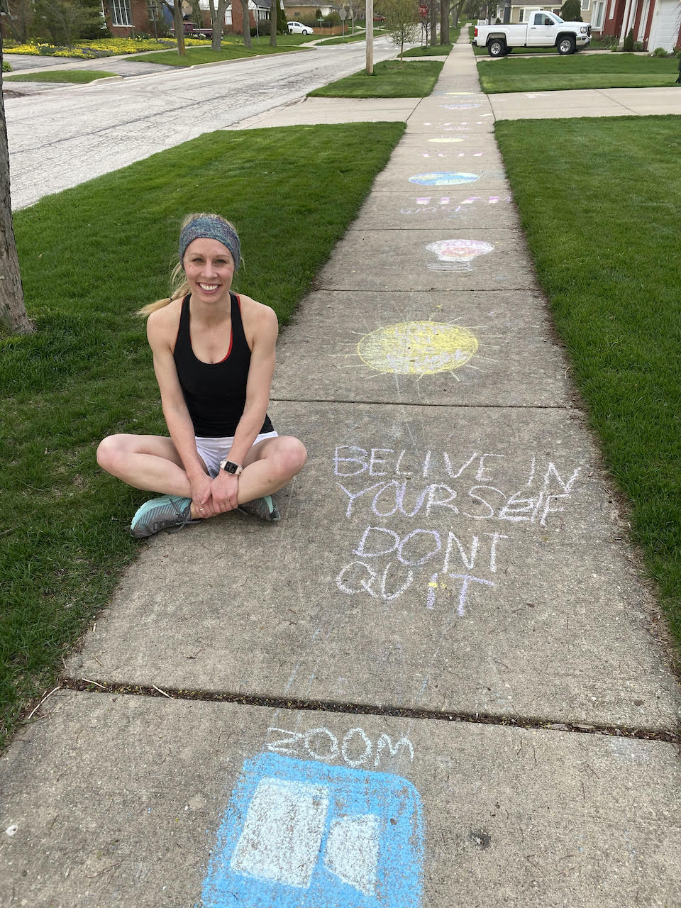 Photo of Beth Ripperger sitting by chalk art that says, "Believe in Yourself."